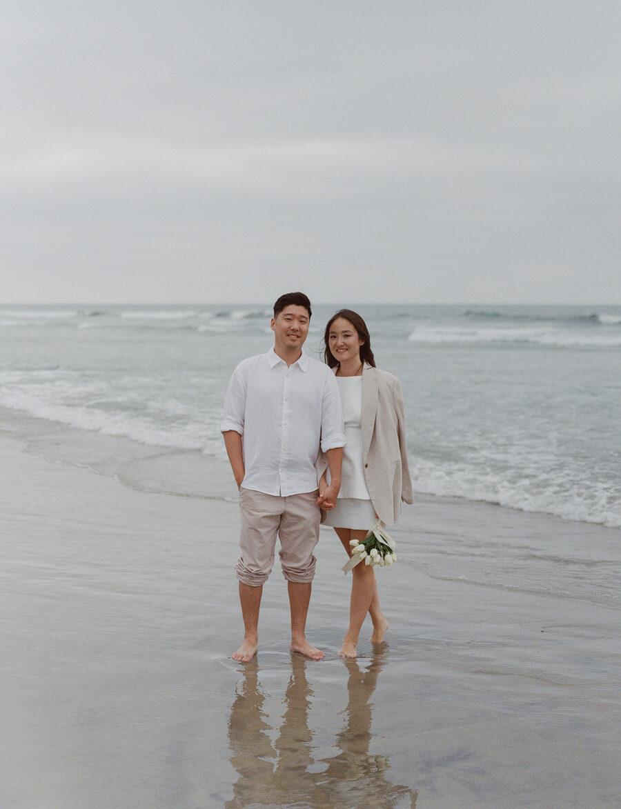 Alice and Matthew holding hands in the surf