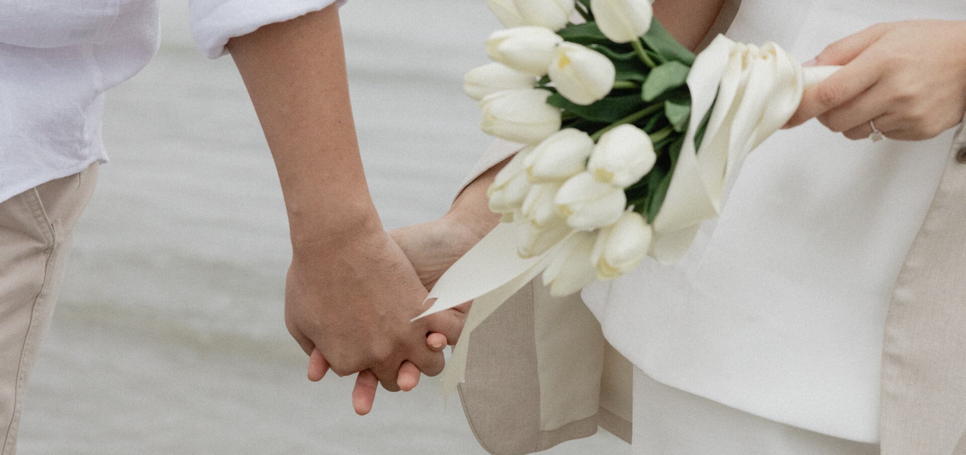 Alice and Matthew holding hands with white tulips on the beach